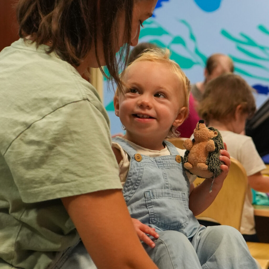 A child sits on an adult's lap holding a plush hedgehog. 